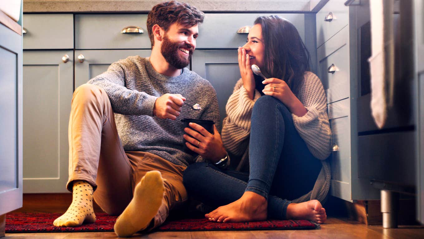 happy young couple sharing a tub of ice cream in their kitchen at home