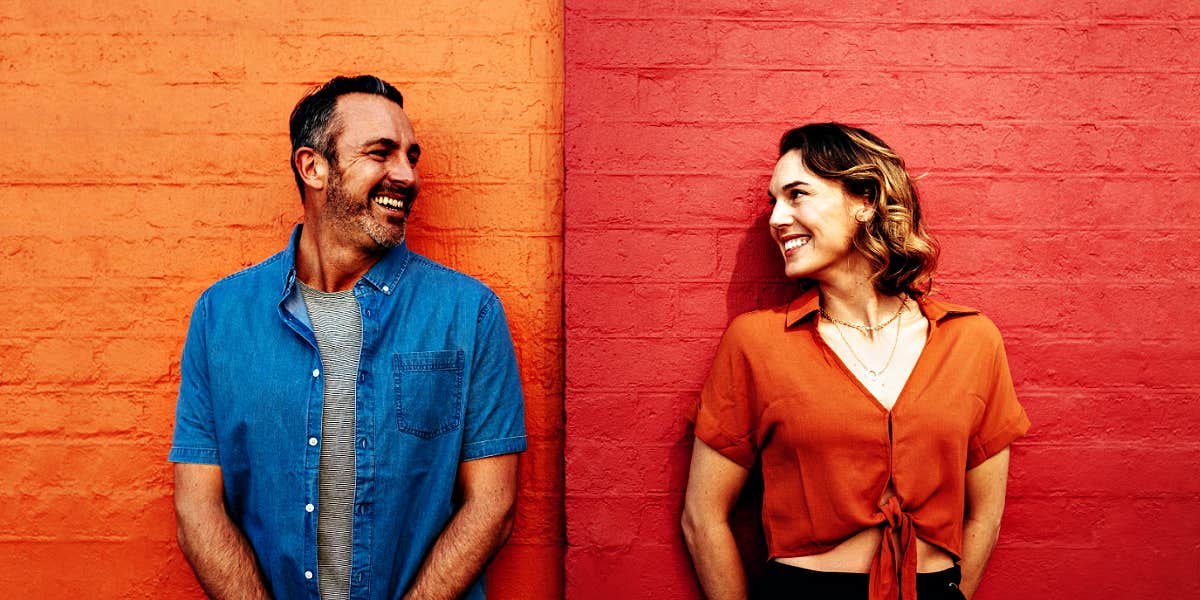 couple standing in front of an orange and red wall, looking at one another