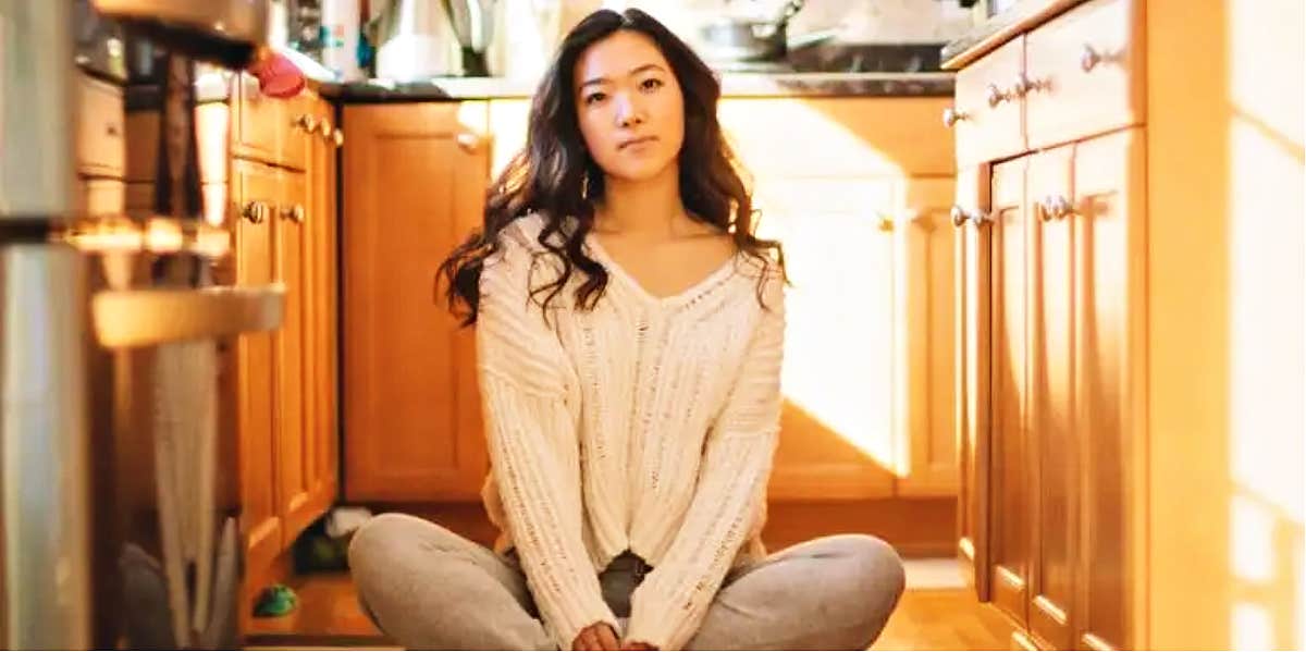 young woman with long dark hair sits on the floor confidently 