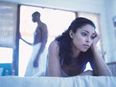 upset woman in bed with man in background
