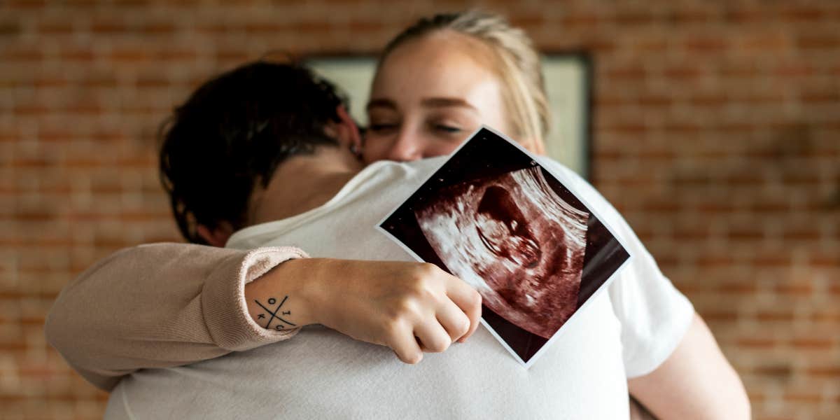 Woman's Husband Suggests Conceiving A Baby With Her Sister The ‘Traditional Way’ Instead Of Surrogacy Couple hugging with ultrasound photo