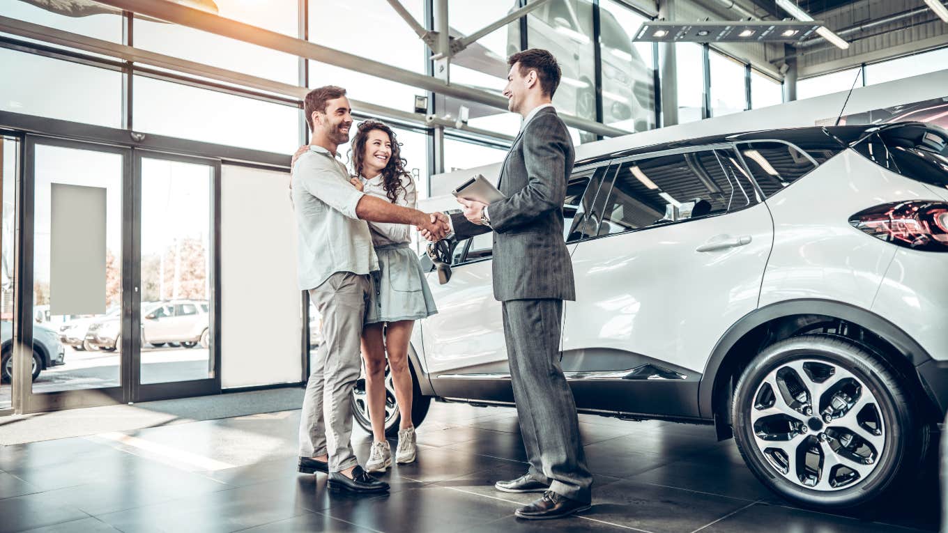 couple shaking hands with car salesman next to SUV