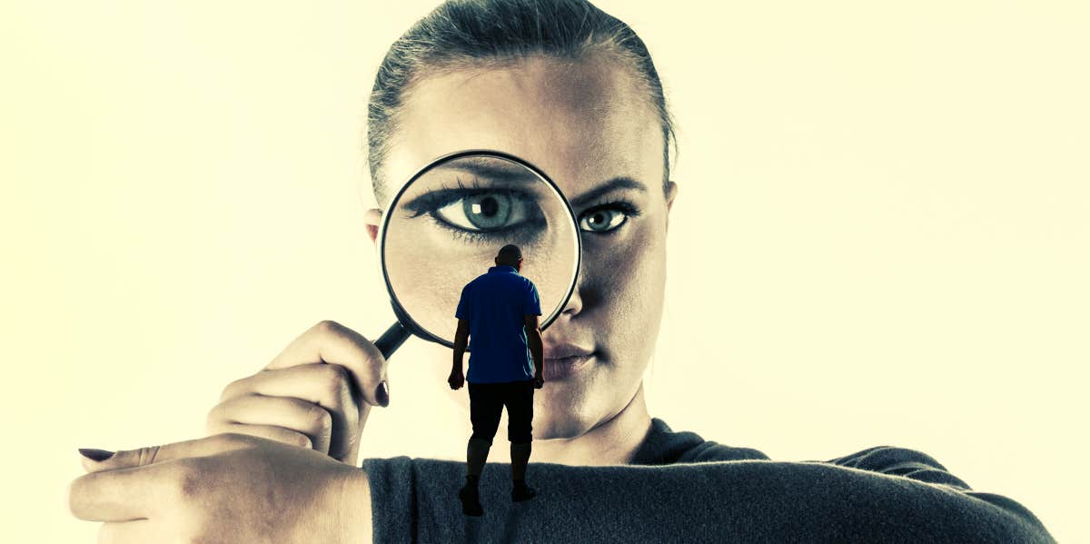 woman peering discerningly through magnifying glass at miniature defeated-looking man