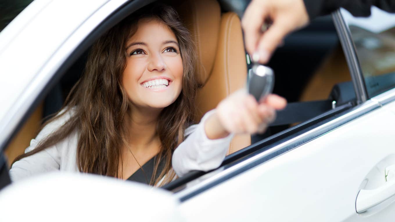 young woman sitting in driver's seat of car being handed key