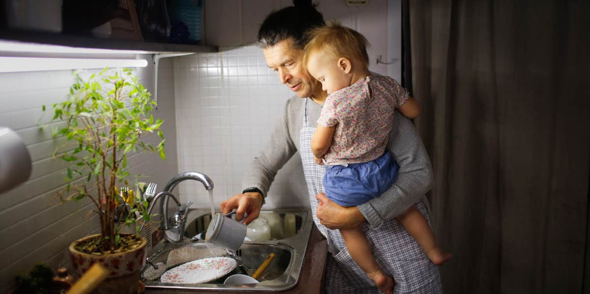 dad washing dishes at the sink while holding baby