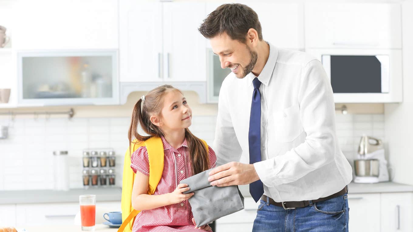 Dad Regrets His Response After Daughter Begs Him To Bring Lunch To School dad handing daughter school lunch in kitchen