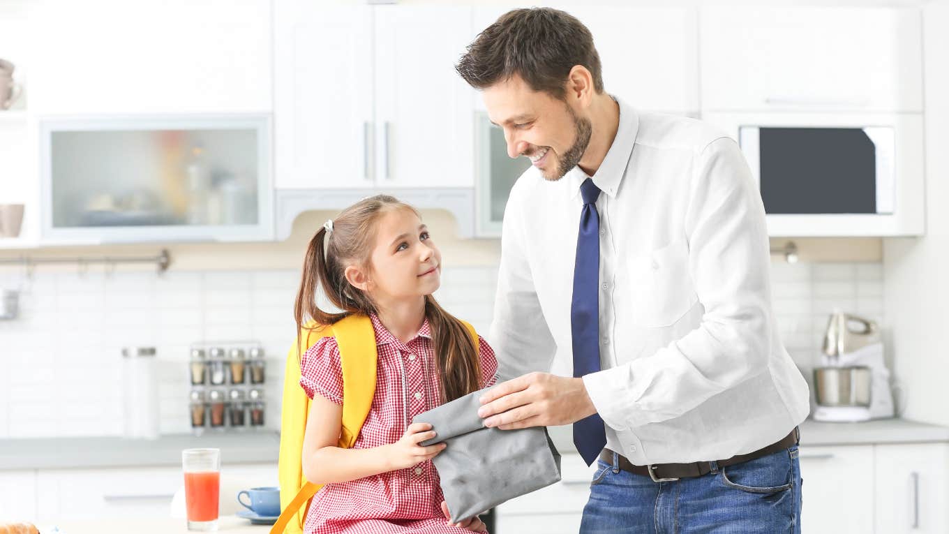 dad handing daughter school lunch in kitchen