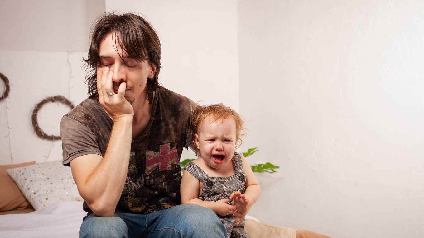 tired dad sitting on couch with screaming baby on his lap