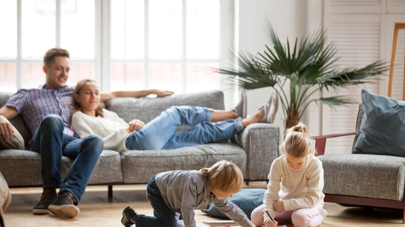 children playing and drawing while sitting on the floor and parents laying on couch