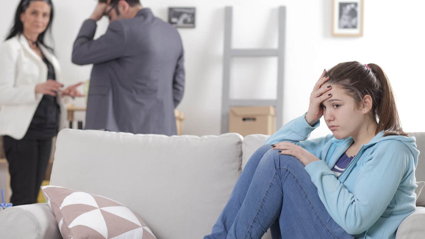upset teen daughter sitting on couch while stressed parents talk behind her