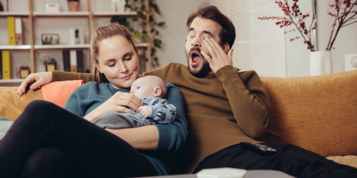 Mother taking care of child while father yawns