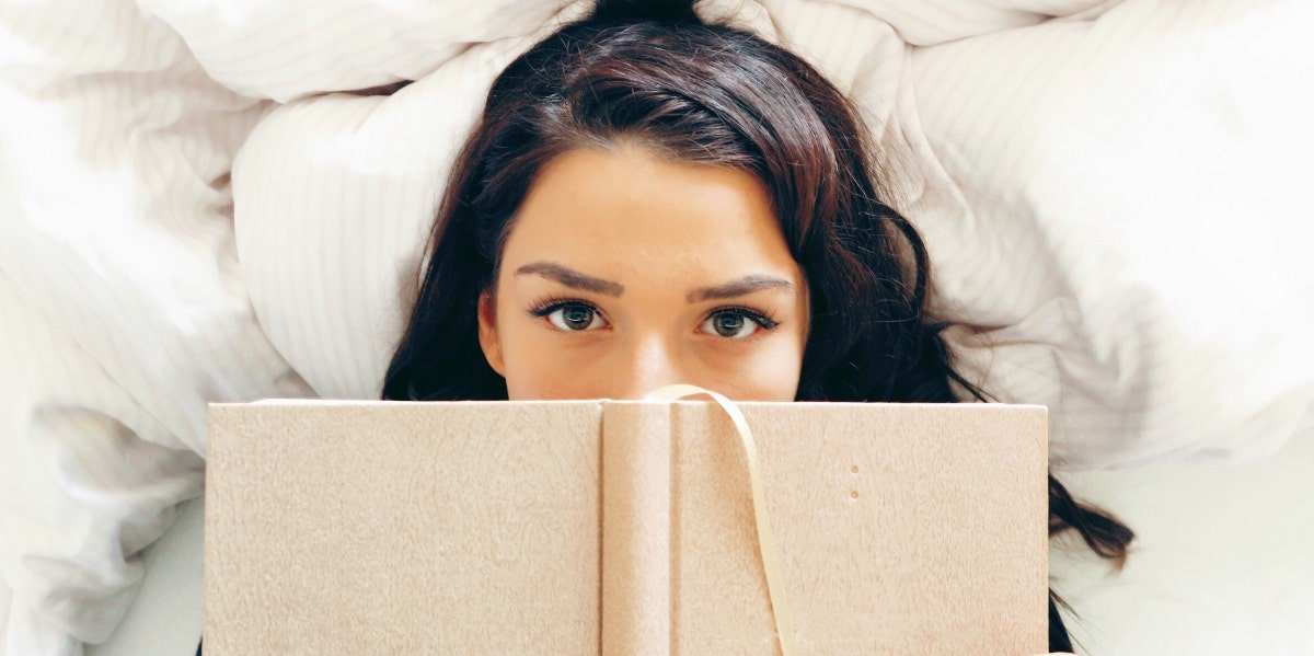 woman lying on bed with book over her face