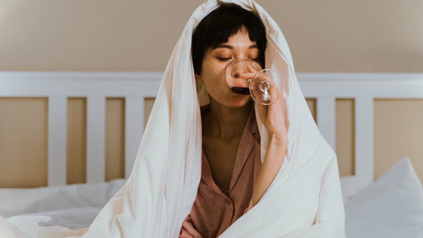 Woman covered by blanket, drinking wine 