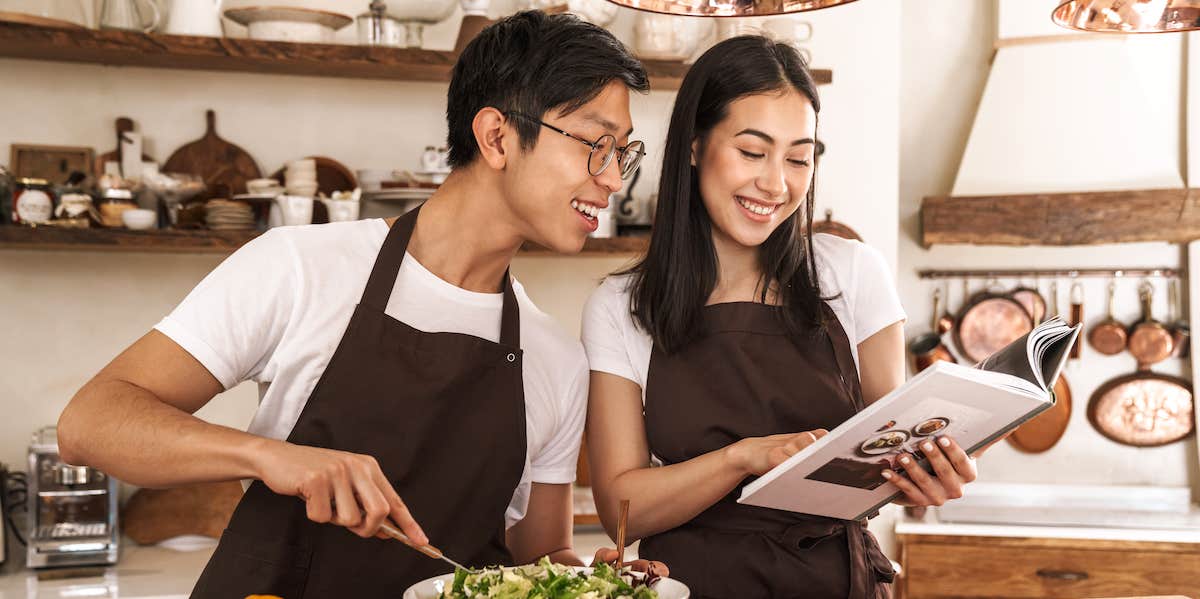 couple smiling and reading recipe book while cooking dinner in cozy kitchen
