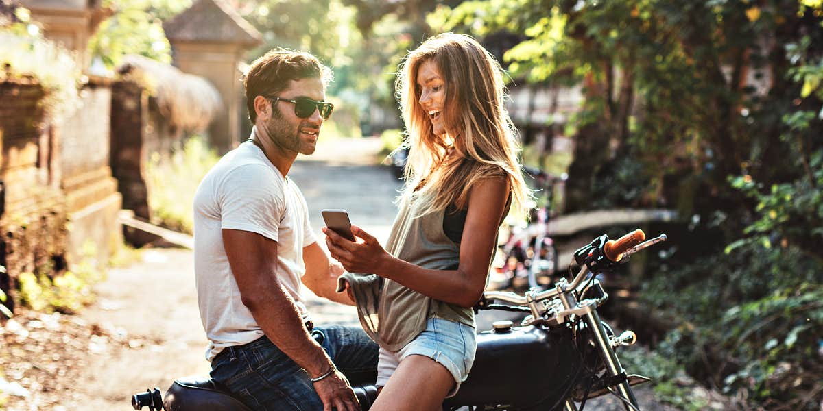 man and woman sitting on a motorcycle on a jungle-like neighborhood road