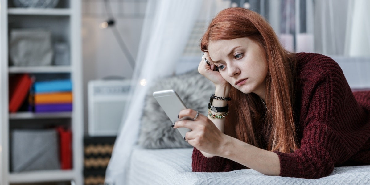 woman lying on bed looking at her phone going through dating burnout