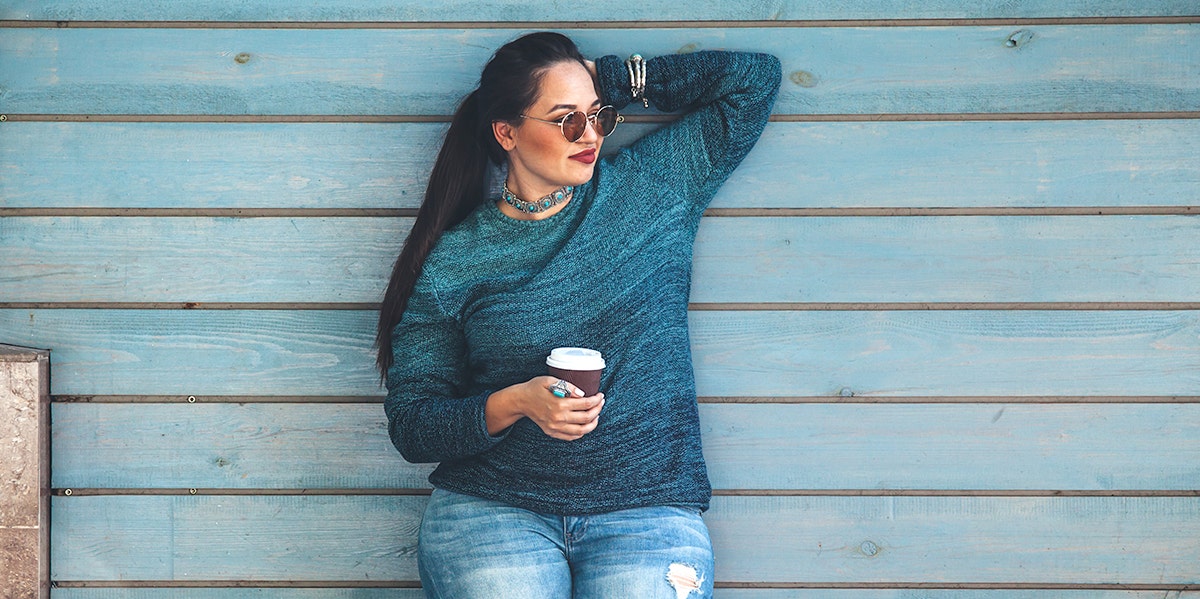 woman holding coffee standing against wall