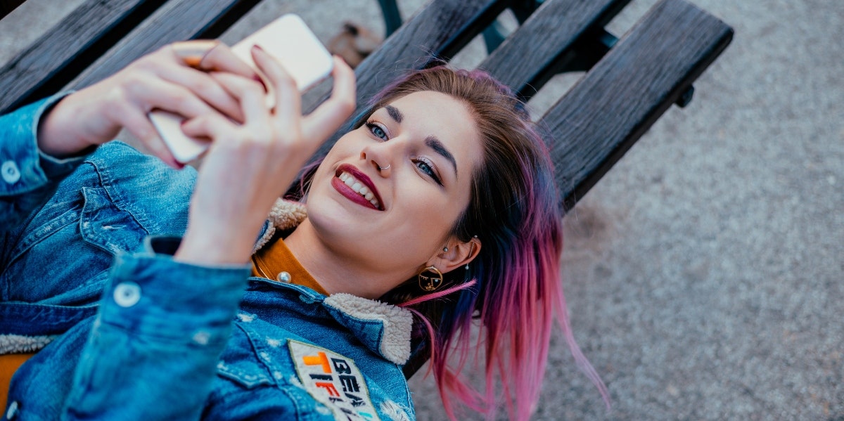 pink-haired woman lying on bench texting