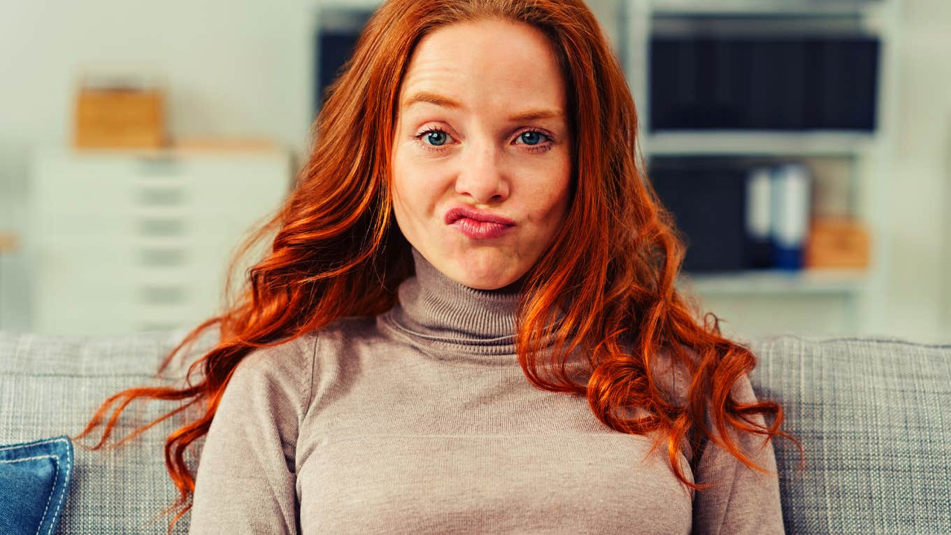 Pretty young redhead woman pulling a funny face making an exaggerated grimace with her lips as she sits on a sofa at home