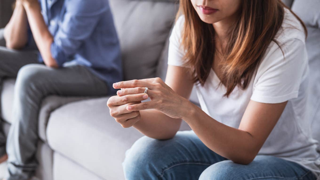 Divorce Coach Shares 4 Reasons Women Are Happier Than Men After A Divorce woman taking off wedding ring while man sits on couch