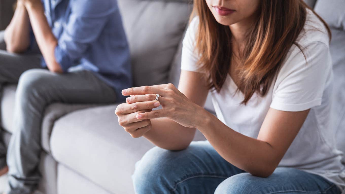 woman taking off wedding ring while man sits on couch