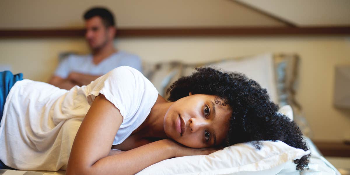 woman laying on bed with husband in background