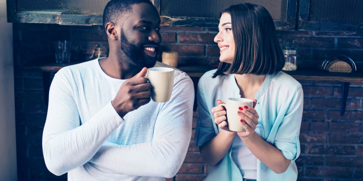 guy and girl looking at each other smiling while holding coffee mugs