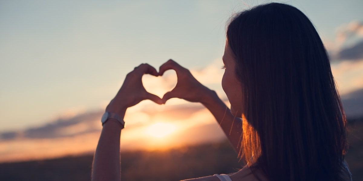 woman making a heart at the sunset