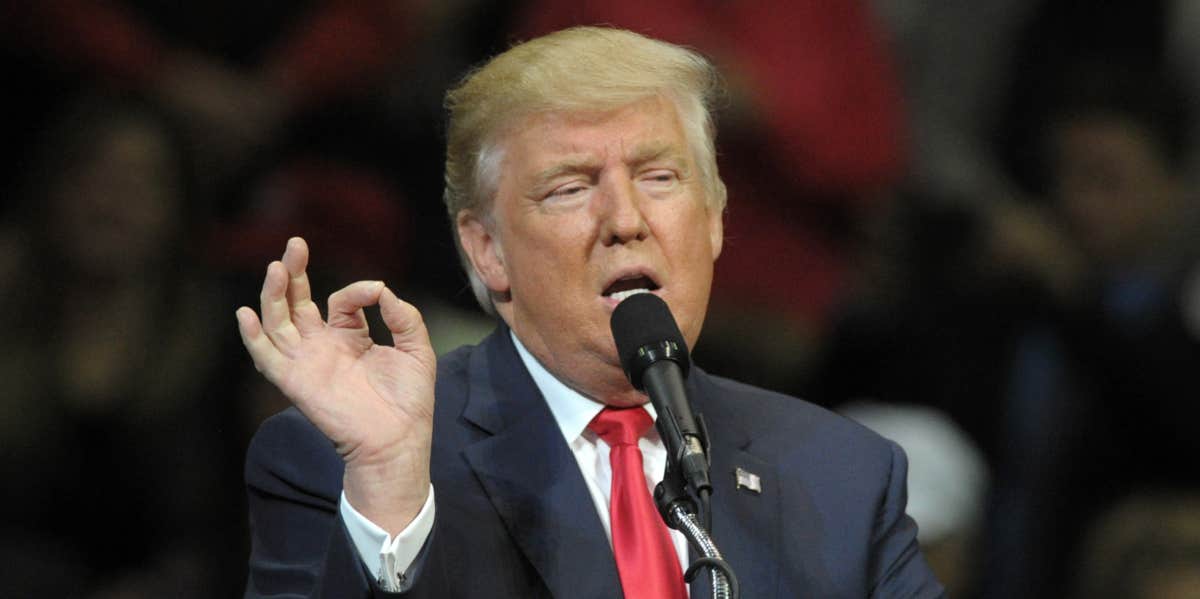 donald trump at a microphone, making a weird gesture