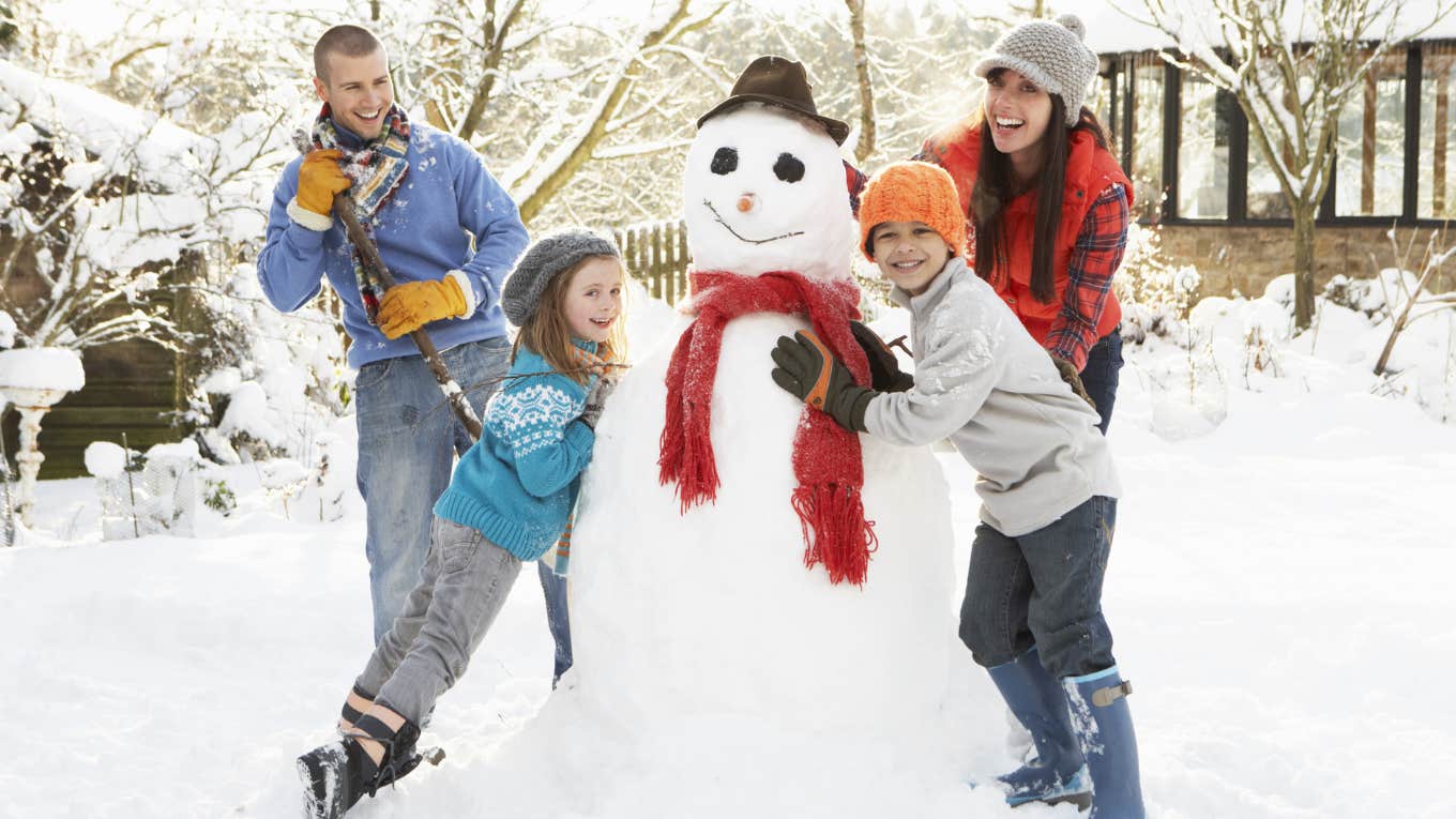 Family smiling outside with their snowman. 