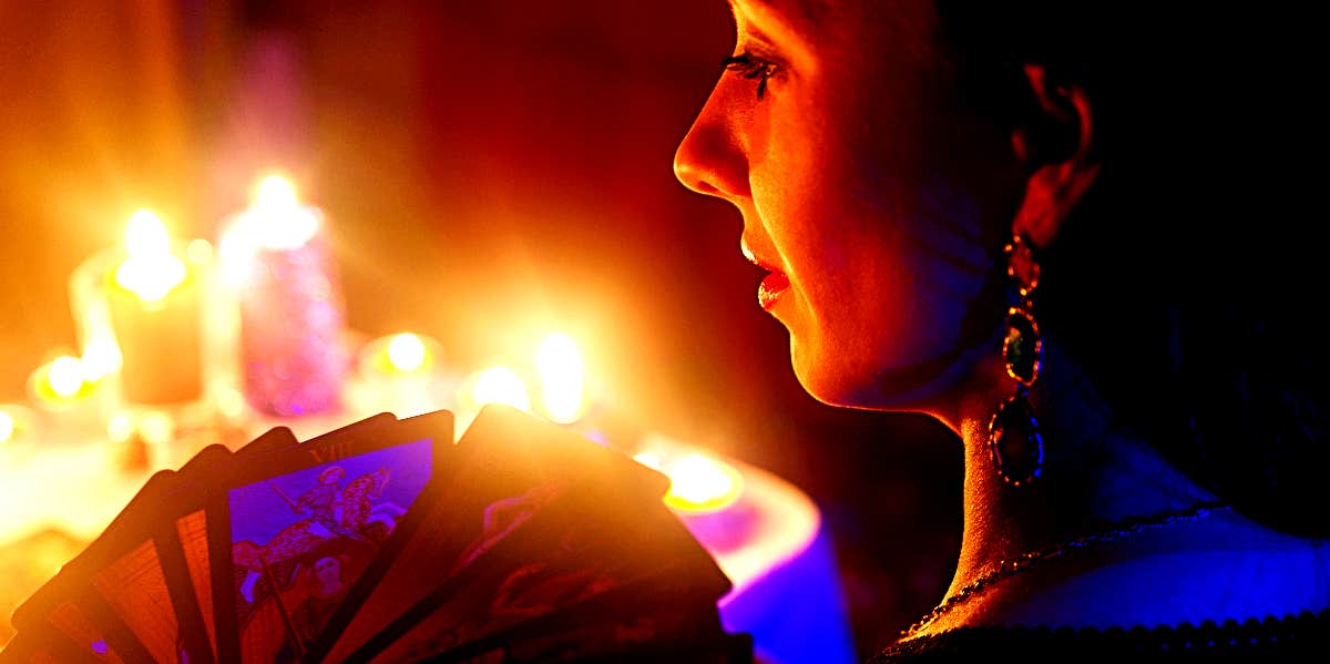 Draw tarot card by hours Woman holds tarot cards in front of candles