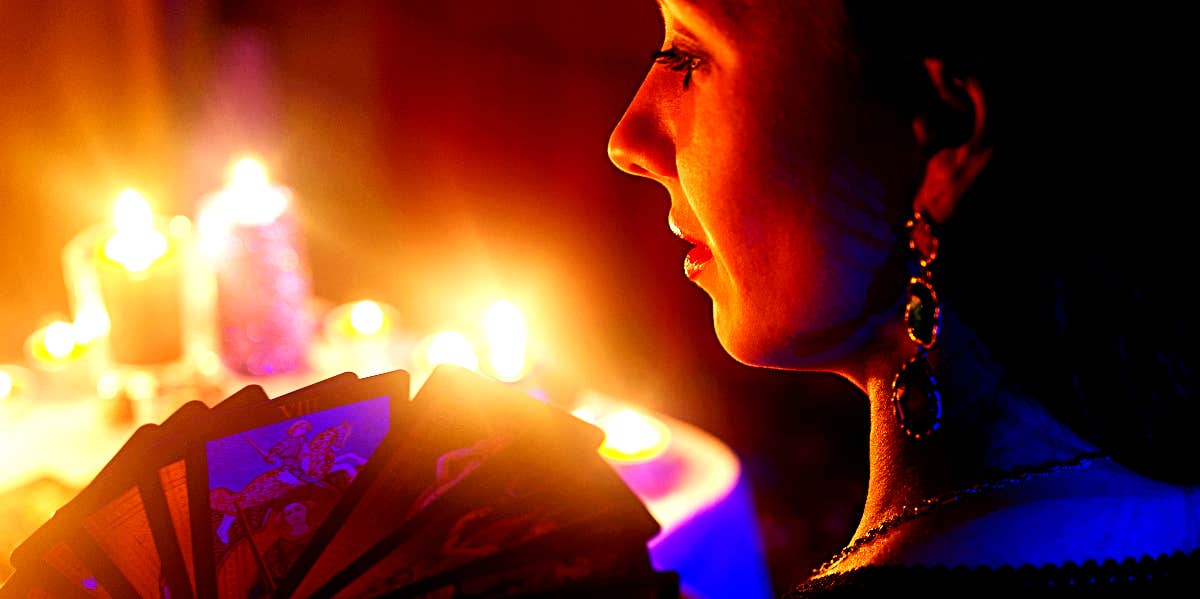 Woman holds tarot cards in front of candles