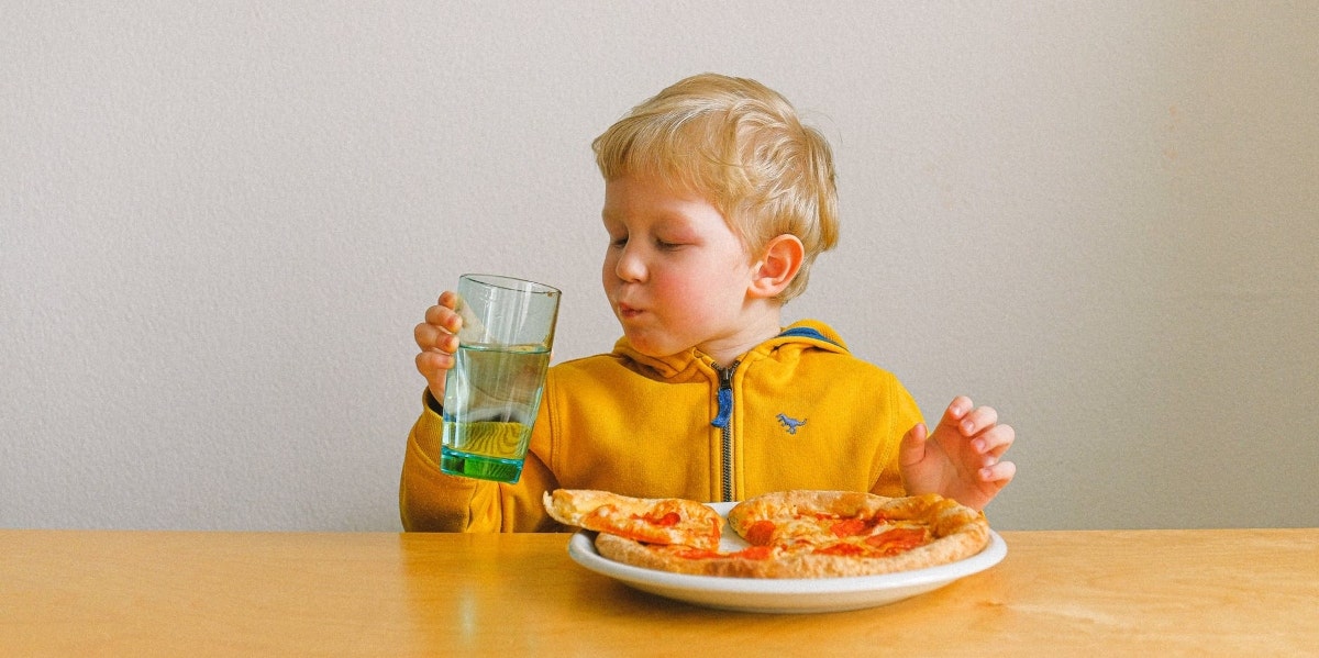 toddler in a yellow shirt eating pizza. 