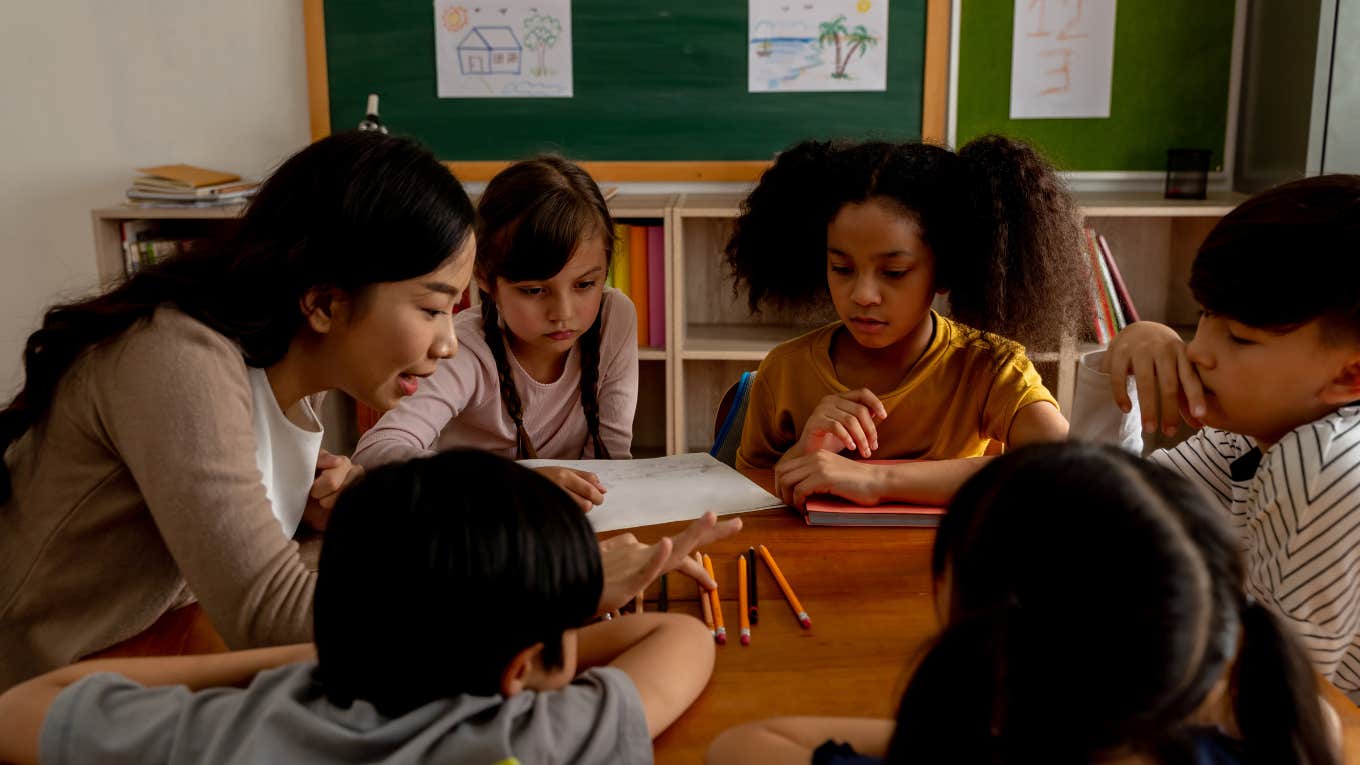 teacher teaching students around desk in classroom