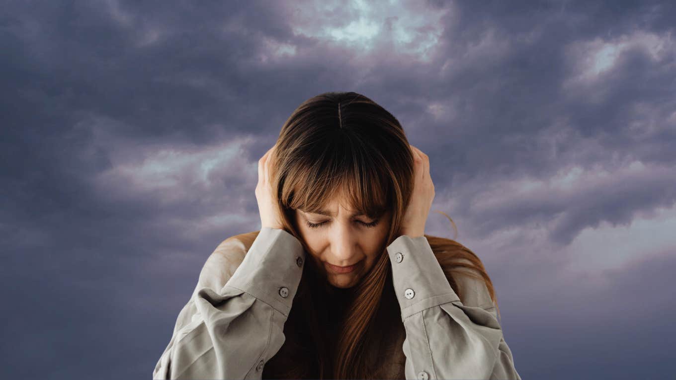 Woman holding her head in front of a dreary background. 