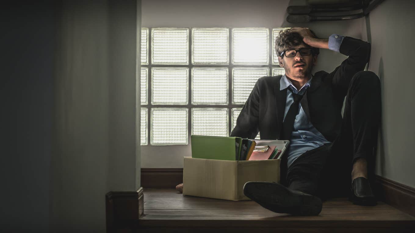 office worker sitting on floor with cardboard box of things in hallway