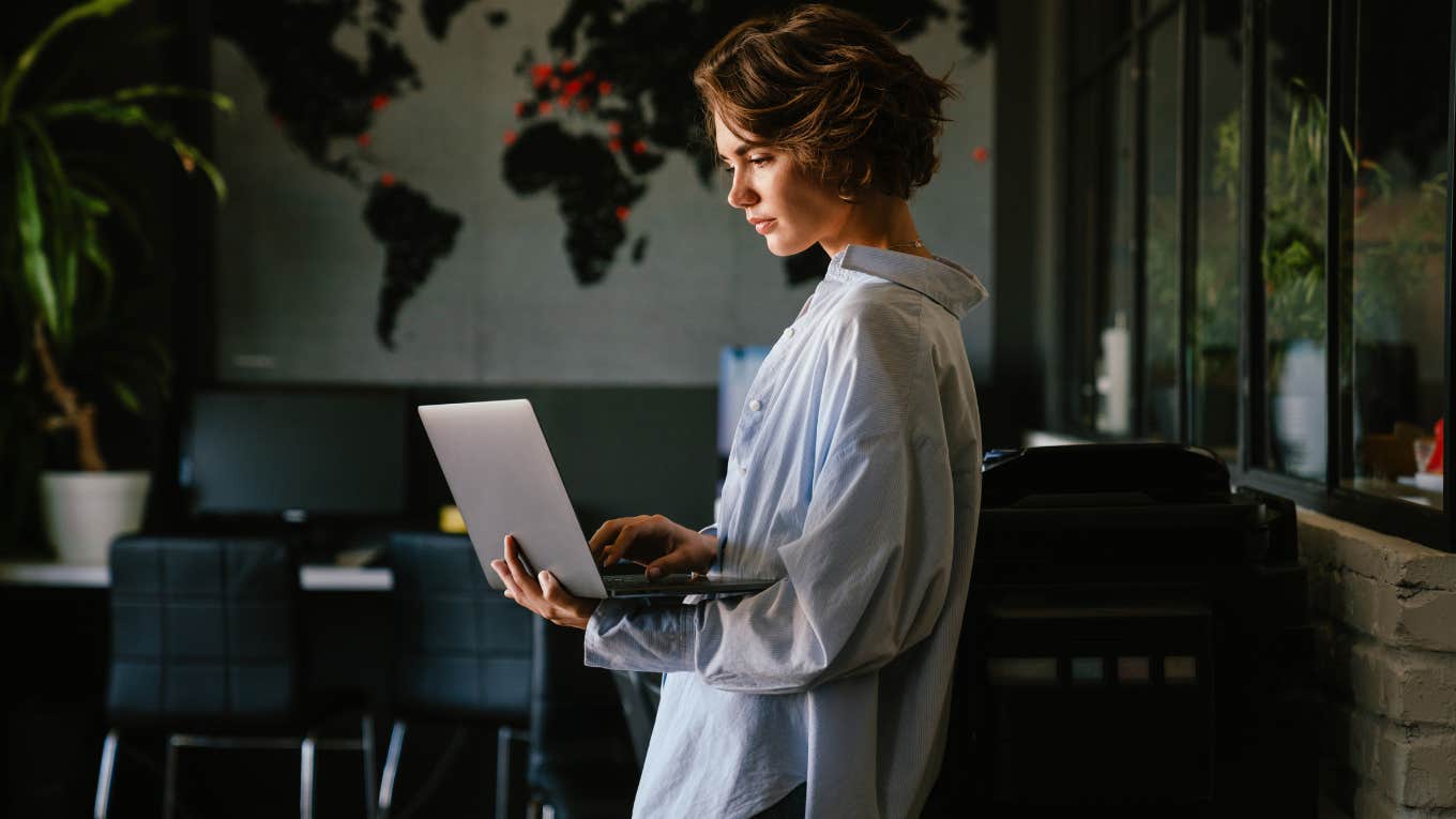 concentrated business woman using laptop while standing in modern workspace