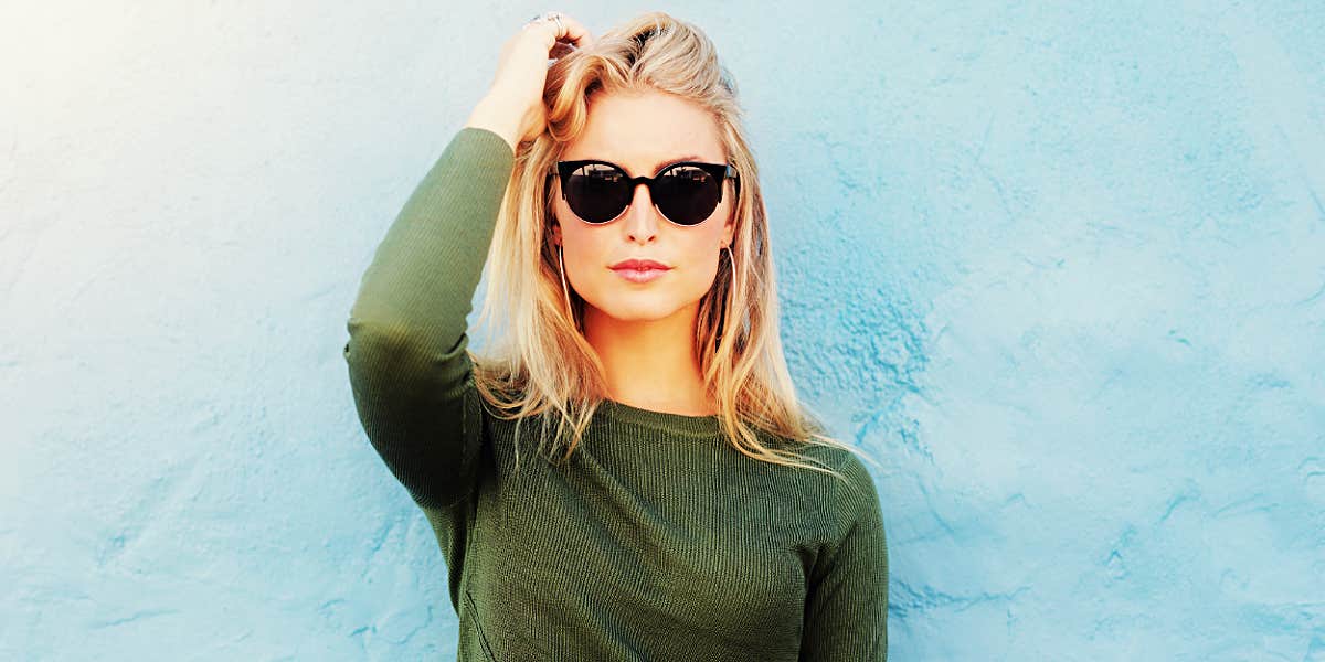 blonde woman in sunglasses against a light blue wall
