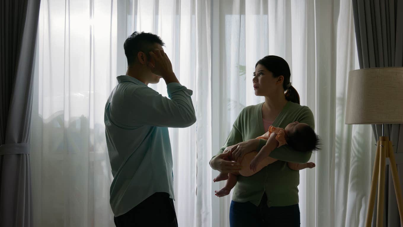 young couple standing by windows with sleeping child are having conflict and argument