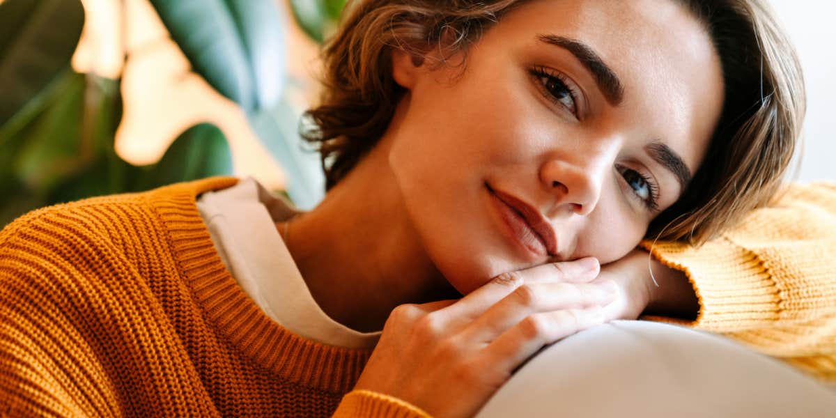 young brunette with a short bob rests cheek on arm, wearing a yellow sweater