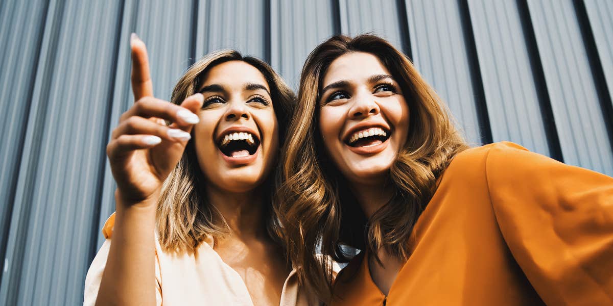 two women laughing in front of a grey wall