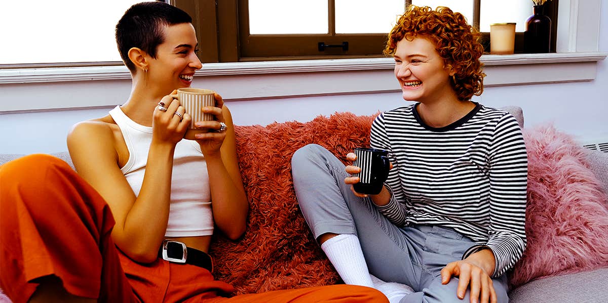 Experts Reveal The Rare Habit That Makes You Infinitely More Likeable two women sitting on couch drinking coffee and chatting