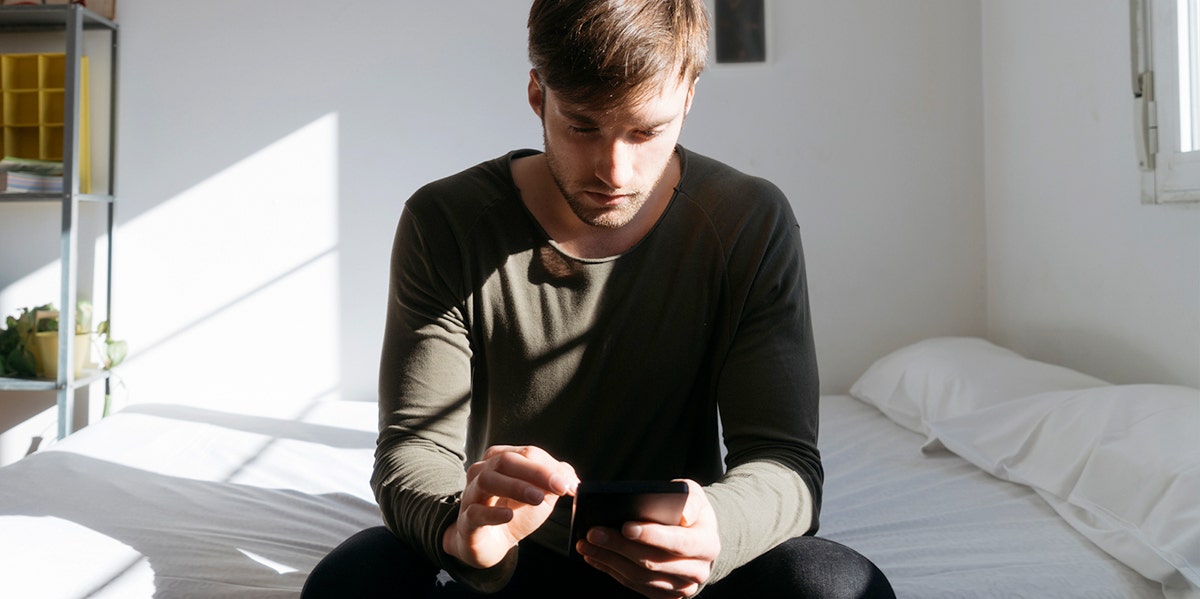 man looking at phone while sitting on bed