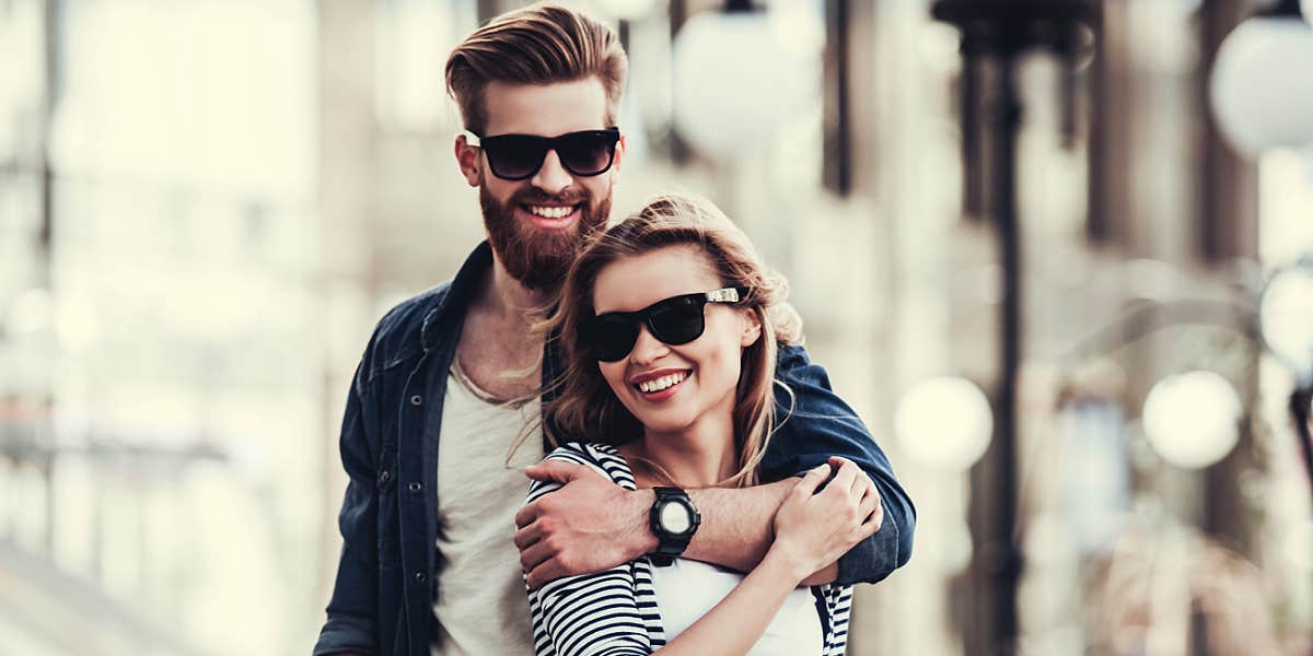Fake good guy gestures man and woman on a street, wearing sunglasses, his arm over her shoulder