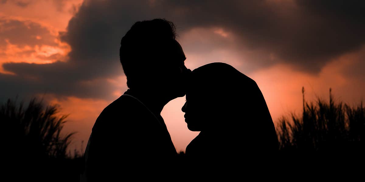 silhouette of man kissing woman's head