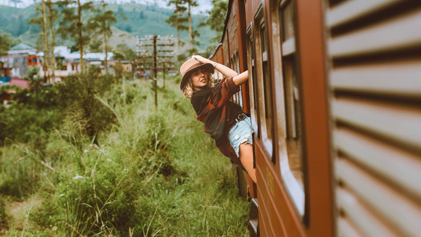  young woman hanging off the side of a train in the countryside
