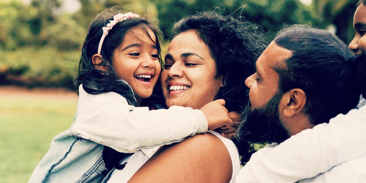 Dad, mom and young daughter hugging while laughing and talking