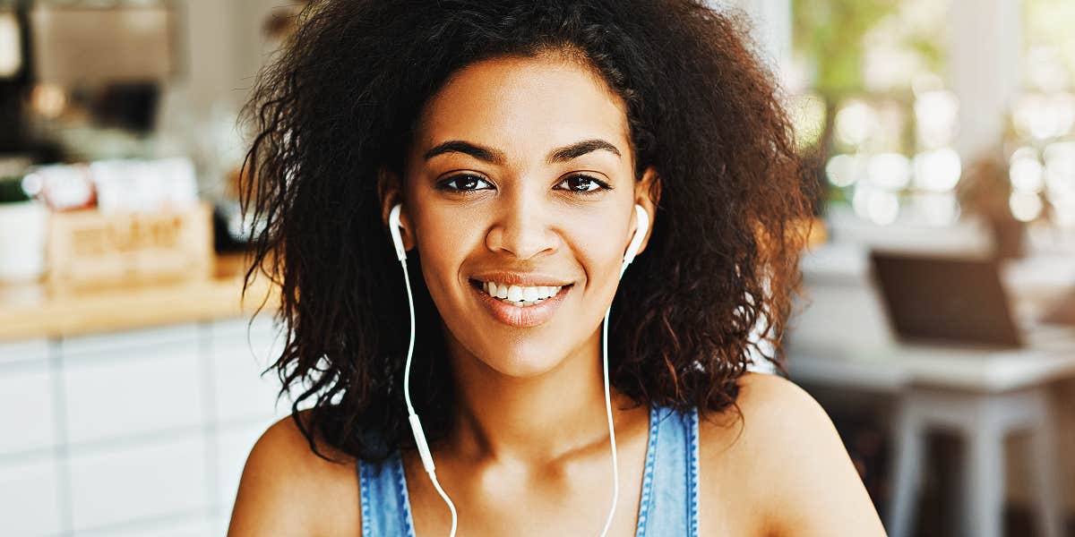 young Black woman smiles in a cafe, wearing earbuds
