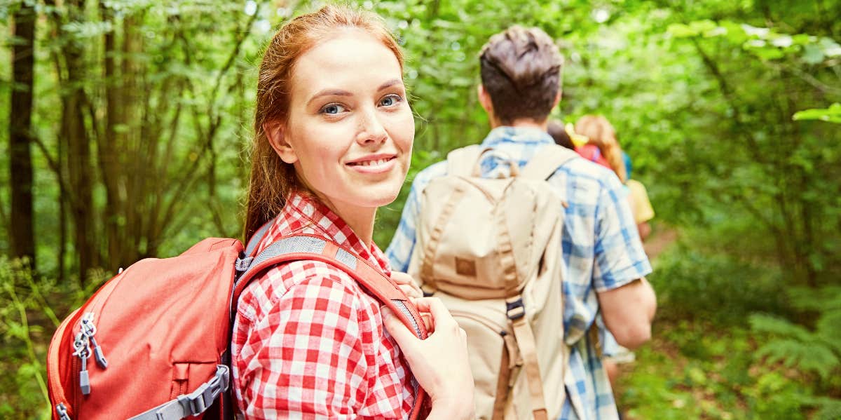 Smiling woman dressed in red hiking through green woods.