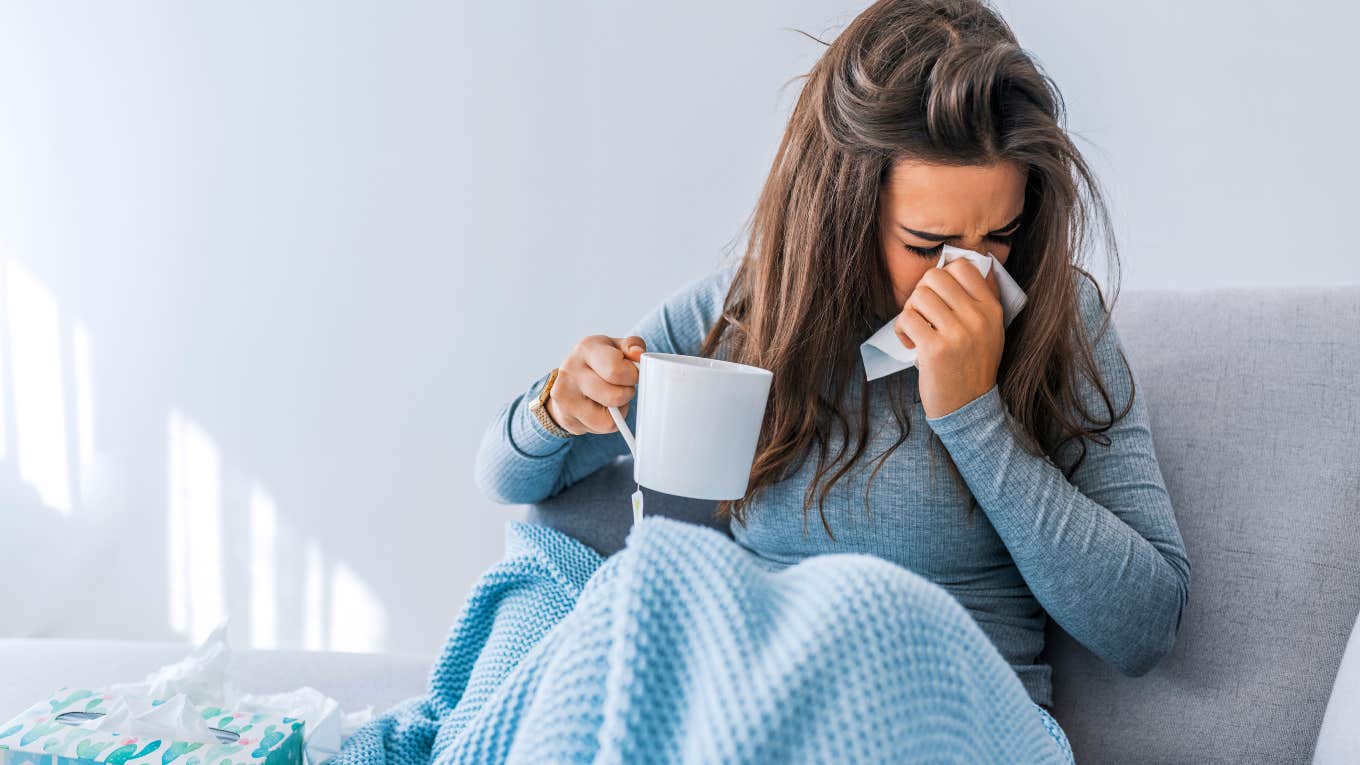 Fitness Instructor Fired Via Group Text For Calling In Sick sick woman on couch with tissues and tea